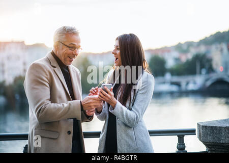 L uomo e la donna business partner con lo smartphone in piedi in città, esprimendo emozione. Foto Stock