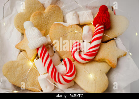 Composizione di natale. Closeup confezione regalo con biscotti di Natale, candy canes e divertenti decorazioni, garland luce su sfondo bianco Foto Stock