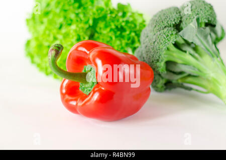 Succosa pepe rosso con una coda verde si trova accanto al fascio di lattuga e broccoli sono su sfondo bianco. isolato Foto Stock