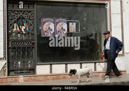 Un vecchio uomo spagnolo a piedi il suo cane passato un negozio che sia chiuso. Foto Stock