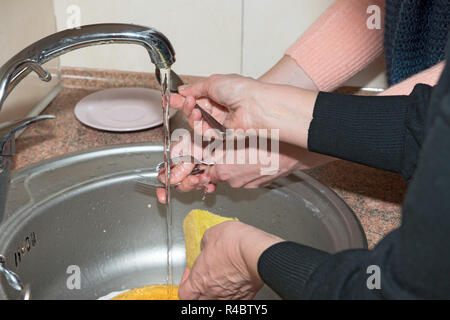 Close-up il lavaggio di stoviglie in quattro donne le mani in acciaio inox con lavello da cucina. Foto Stock