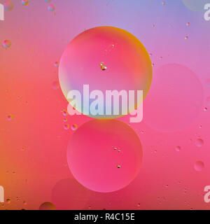 Artistico foto macro di goccioline di olio galleggiante sull'acqua con uno sfondo colorato Foto Stock