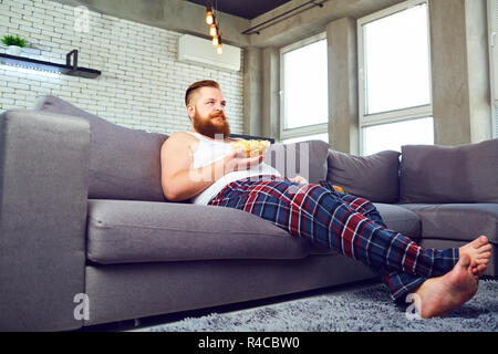 Spesso l'uomo barbuto popcor mangiare seduti sul divano. Foto Stock