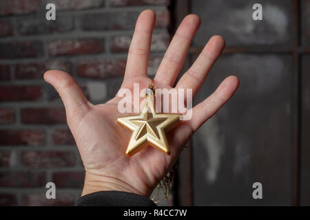 Golden stella a cinque punte decorazione in mani su sfondo scuro. Foto Stock