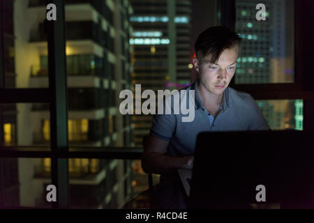 Giovane uomo bello utilizzando laptop contro il vetro della finestra con vista o Foto Stock