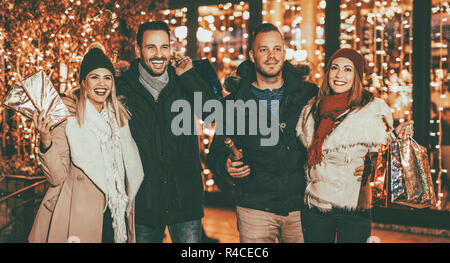 Il gruppo di un felice giovani godendo di shopping nel centro commerciale per lo shopping con un luminoso negozio finestra in background. Essi sono il trasporto delle borse della spesa e scatole. Foto Stock