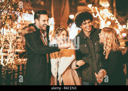 Allegro quattro amici divertendosi in città strada nella notte di Natale, parlare di qualcosa di divertente. Foto Stock