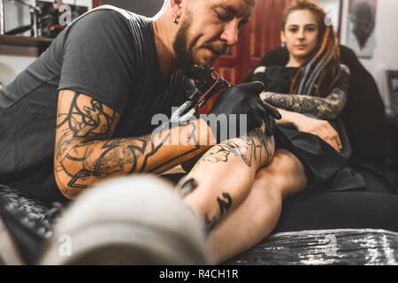 Ragazza con dreadlocks in un salotto tattoo. Il master crea un'immagine del corpo di una giovane ragazza bella. Close-up di mani e tattoo machine Foto Stock