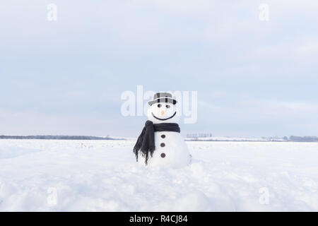 Divertente pupazzo di neve in elegante cappello e scalf nero sul campo nevoso Foto Stock