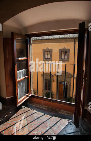 Vista da una finestra del castello: flussi di luce su un pavimento di pietra attraverso una finestra che si affaccia sul cortile interno di un castello in Toscana. Foto Stock