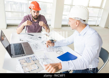 Gli ingegneri di sesso maschile, gli architetti che lavorano presso il desk di caschi. Disegni, laptop, roulette sul desktop. La reception e la supervisione della costruzione di constructi Foto Stock