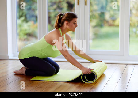 Una donna che stende un tappetino yoga Foto Stock