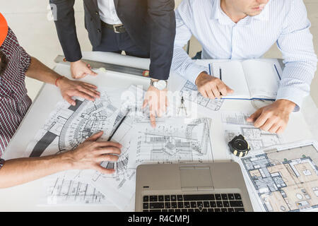 Gli ingegneri di sesso maschile, gli architetti che lavorano presso il desk di caschi. Disegni, laptop, roulette sul desktop. La reception e la supervisione della costruzione di constructi Foto Stock