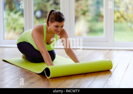 Una donna che stende un tappetino yoga Foto Stock