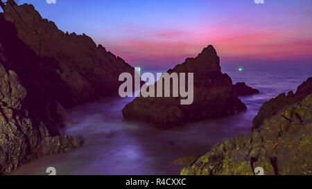 Le onde battono il grande cono roccia al centro di pietre cape durante il tramonto al Banana beach Phuket Foto Stock