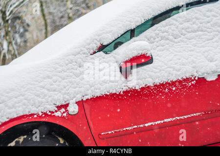 Frammento di auto rossa coperta con uno spesso strato di neve. Inverno sfondo meteo Foto Stock