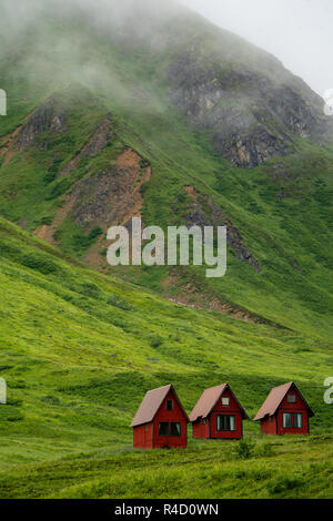 Abbandonate le cabine rosso sedersi nel verde delle lussureggianti montagne di Alaska's Hatcher passano vicino alla miniera di indipendenza. Foto Stock