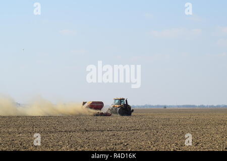 Il trattore corre sul campo e rende il fertilizzante nel terreno. Fertilizzanti dopo aratura del campo. Foto Stock