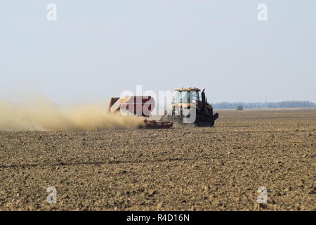 Il trattore corre sul campo e rende il fertilizzante nel terreno. Fertilizzanti dopo aratura del campo. Foto Stock