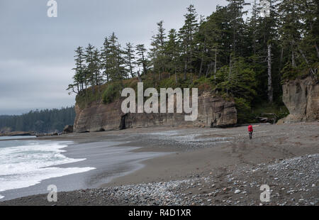 Donna trekking lungo una spiaggia con uno zaino sulla West Coast Trail. Foto Stock