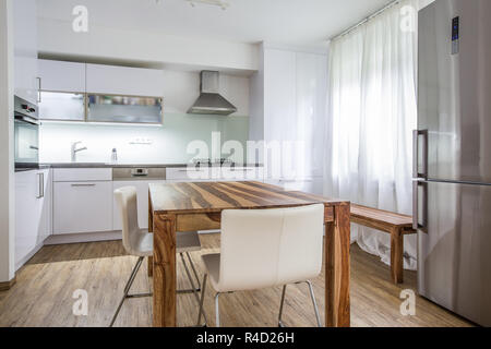 Cucina moderna Interior Design Architettura magazzino l'immagine, la foto di una moderna cucina bianca con un legno scuro tavolo, hi-end apparecchi e abbondanza di luce diurna Foto Stock