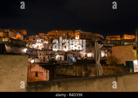 La città antica di Matera, Italia, con un campanile di una chiesa nascente in mezzo alle colline abbandonate case e ben illuminata e negozi a tarda notte in Basilicata ri Foto Stock