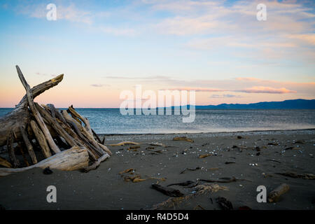 Le sfumature del tramonto su orizzonte con driftwood shelter su Collingwood spiaggia di Isola del Sud della Nuova Zelanda Foto Stock