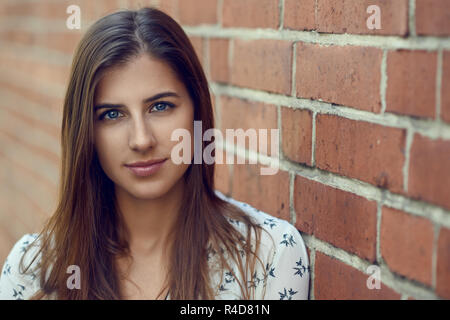 Ritratto di giovane bella bruna donna con cordiale bella faccia, in camicia bianca, guardando la telecamera mentre sta in piedi vicino al red muro di mattoni con copia Foto Stock