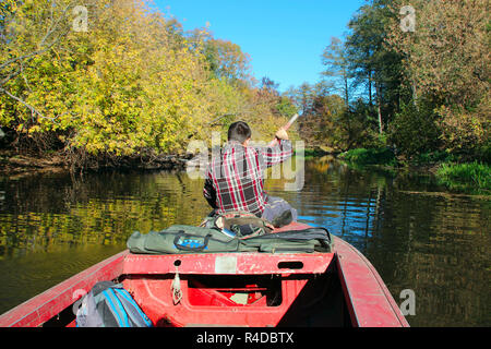 Pescatore sulla vela barca sul fiume in autunno. Fisherman con paddle galleggianti lungo il fiume con una fitta vegetazione lungo le rive. Uomo di andare in barca Foto Stock
