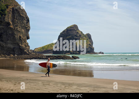 Uomo con una tavola da surf a Piha Beach, Nuova Zelanda Foto Stock