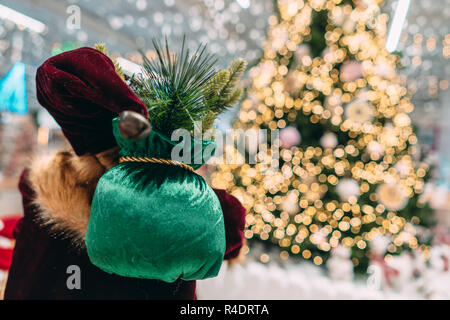 Santa da dietro con borsa regalo su sfondo bokeh di albero di natale. Foto Stock