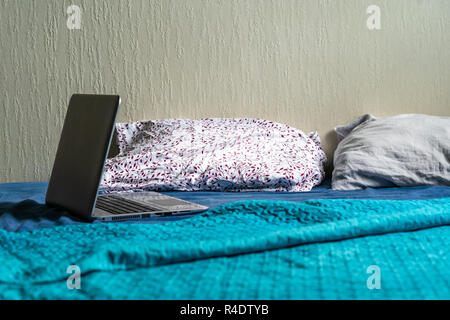 Grigio Laptot posa sul materasso con coperchio color turchese, alcuni cuscini e uno sfondo bianco - per gli studenti degli studi Foto Stock
