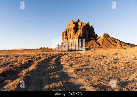 La curvatura della strada attraverso un vasto paesaggio per la formazione rocciosa di Shiprock nel Nuovo Messico Foto Stock