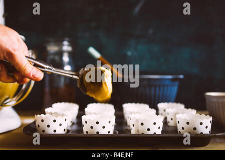 Muffin sono versata nella tazza di camicie pronte per essere cucinate in forno durante la preparazione di qualche muffin di zucca di Halloween sono visualizzati su un blu r Foto Stock