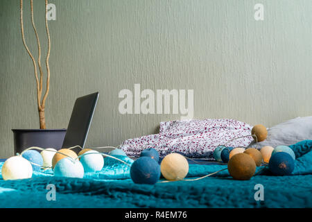 Grigio Laptot posa sul materasso con coperchio color turchese, alcuni cuscini e uno sfondo bianco - con un impianto in camera oltre ad esso e decorazione di Natale Luci Foto Stock