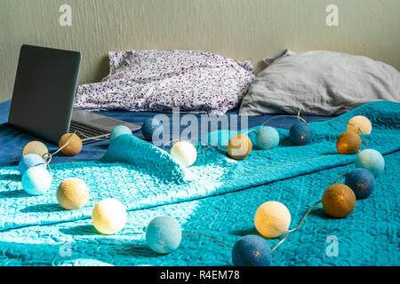Grigio Laptot posa sul materasso con coperchio color turchese, alcuni cuscini e uno sfondo bianco - con decorazione di Natale luci sul letto Foto Stock