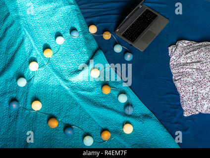 Grigio Laptot posa sul materasso con coperchio color turchese, alcuni cuscini e uno sfondo bianco - con decorazione di Natale luci sul letto Foto Stock