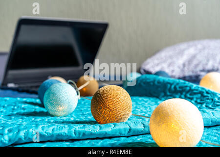 Grigio Laptot posa sul materasso con coperchio color turchese, alcuni cuscini e uno sfondo bianco - con decorazione di Natale luci sul letto Foto Stock