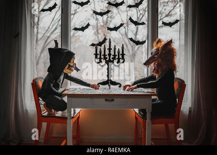 Due bambini in costumi di Halloween seduto da una finestra facendo un puzzle, Stati Uniti Foto Stock