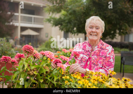 Senior donna ammirando fiori nel giardino Foto Stock
