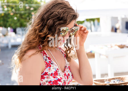 Primo piano della giovane donna shopping per i moderni occhiali da sole brillante cercando nel mercato outdoor shop store in Florida città, villaggio in una colorata estate Foto Stock