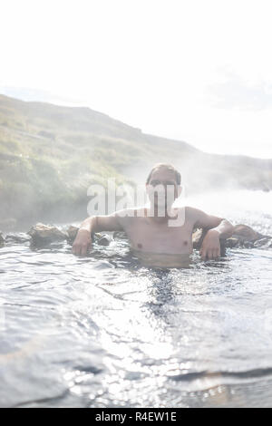 Giovane uomo felice nuoto balneazione in Hveragerdi Hot Springs sul sentiero in Reykjadalur, durante la stagione autunnale mattinata estiva giorno nel sud dell'Islanda, Golden Circle, Foto Stock