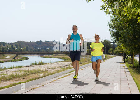 Colpo di giovane donna e uomo che corre attraverso il riverside via Foto Stock