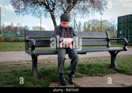 Regno Unito, bambino seduto da solo su una panchina nel parco, sensazione di bullismo Foto Stock
