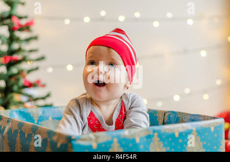 Felice Natale Baby girl in un presente casella intorno all albero di Natale e decorazioni Foto Stock