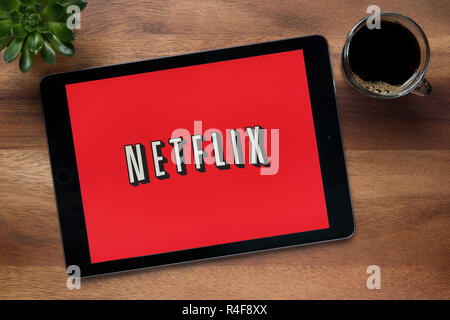 Il sito web di Netflix è visto su un tablet iPad, su di un tavolo di legno lungo con un caffè espresso e una pianta di casa (solo uso editoriale). Foto Stock