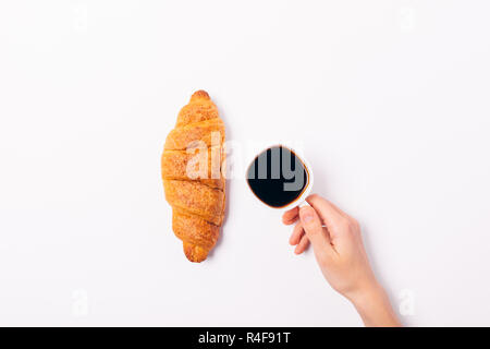 Vista da sopra deliziosi croissant croccante e la tazza di caffè nero nella donna la mano sul tavolo bianco, minima piana composizione laici della prima colazione. Foto Stock