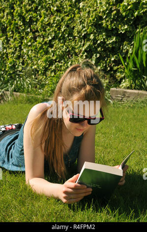 Ragazza adolescente la lettura di un libro che giace nel giardino in estate. Foto Stock