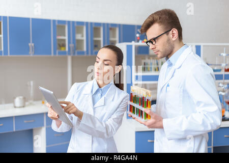 Giovane donna scienziato che mostra digitale compressa al collega tenendo le provette per la prova Foto Stock