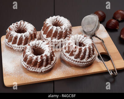 Miniatura Bundt di castagne torte con scaglie di cioccolato su un bambù tagliere, al buio su un sfondo marrone Foto Stock